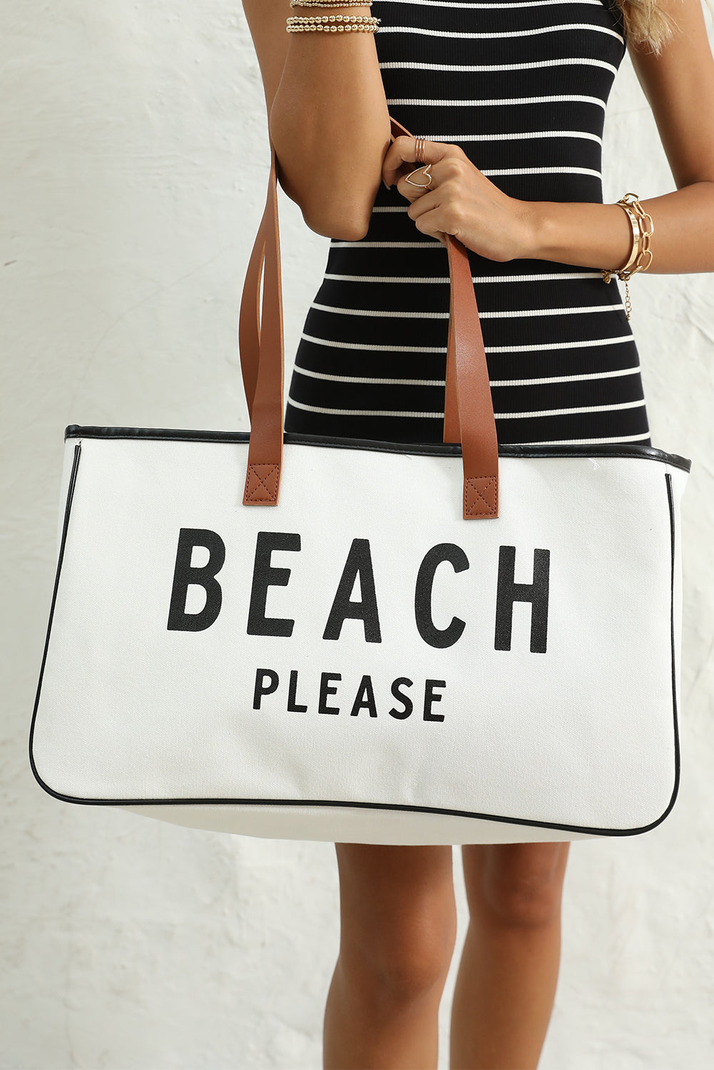 Person holding a tote bag with 'Beach Please' text against a neutral background